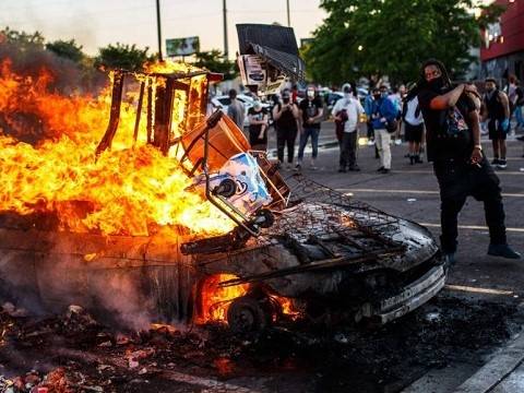 a protester stands next to a burning police car during the george floyd riots in minnesota