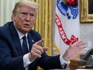 donald trump pointing at the camera while sitting next to phones at his desk