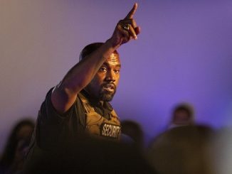 kanye west in a bullet proof vest pointing to the sky in his first presidential rally of 2020