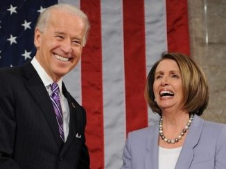 smiling joe biden standing next to smiling nancy pelosi in front of an american flag